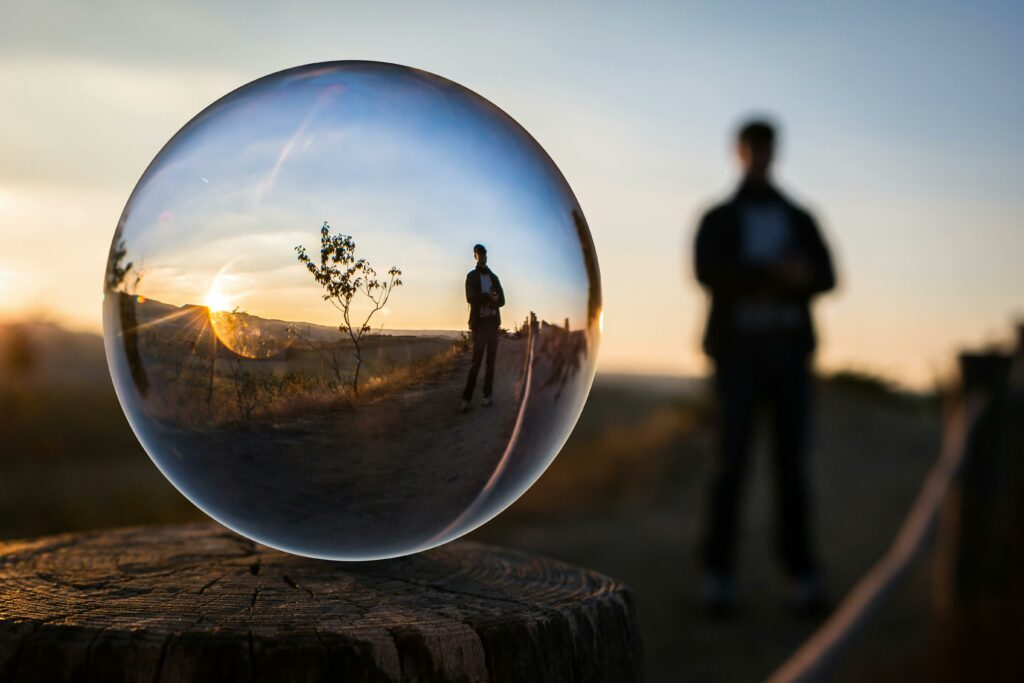 A stunning sunset captured through a glass sphere, showcasing a reflection of a standing silhouette.