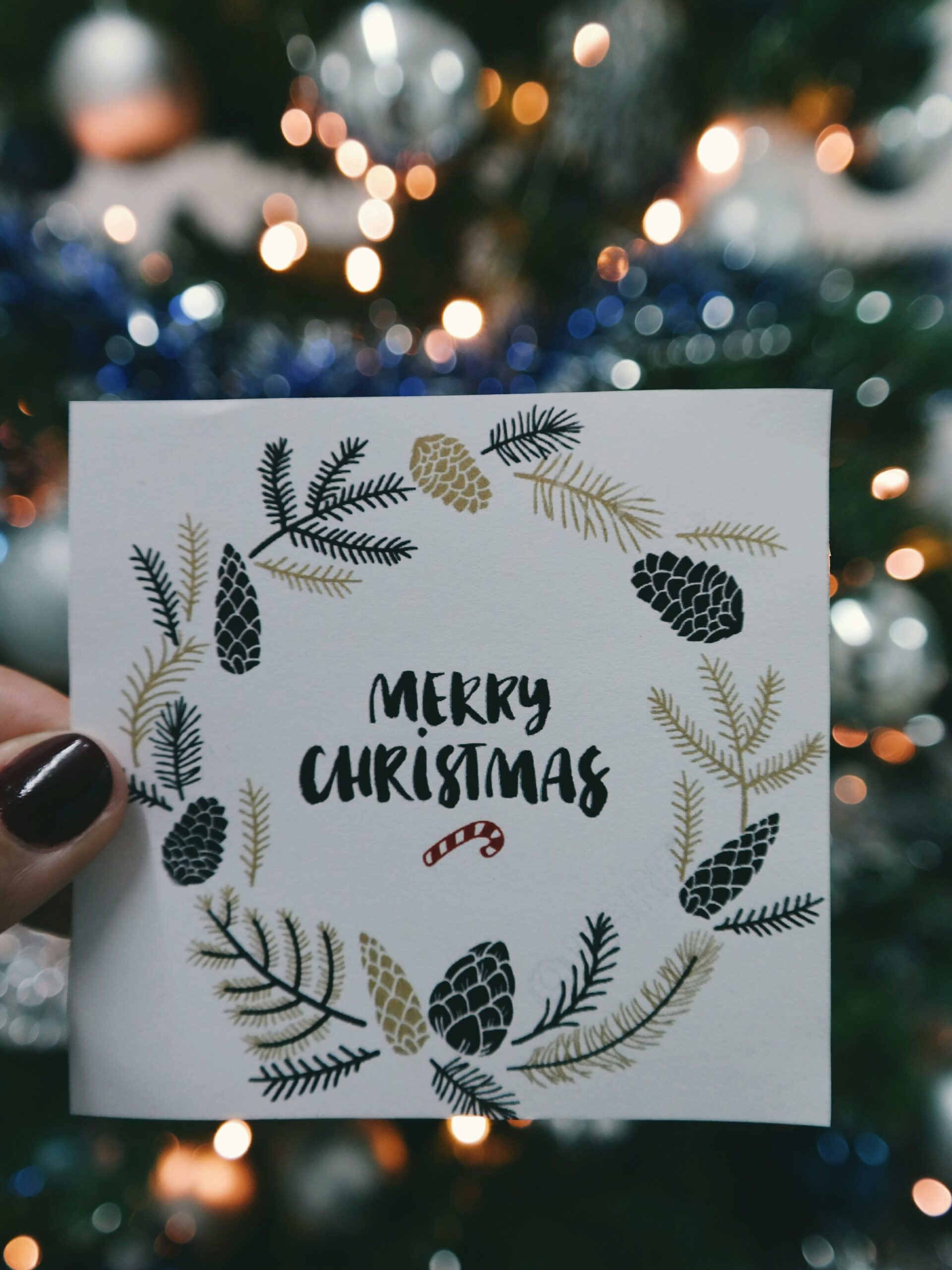 Merry Christmas card held in front of decorative tree with bokeh lights.