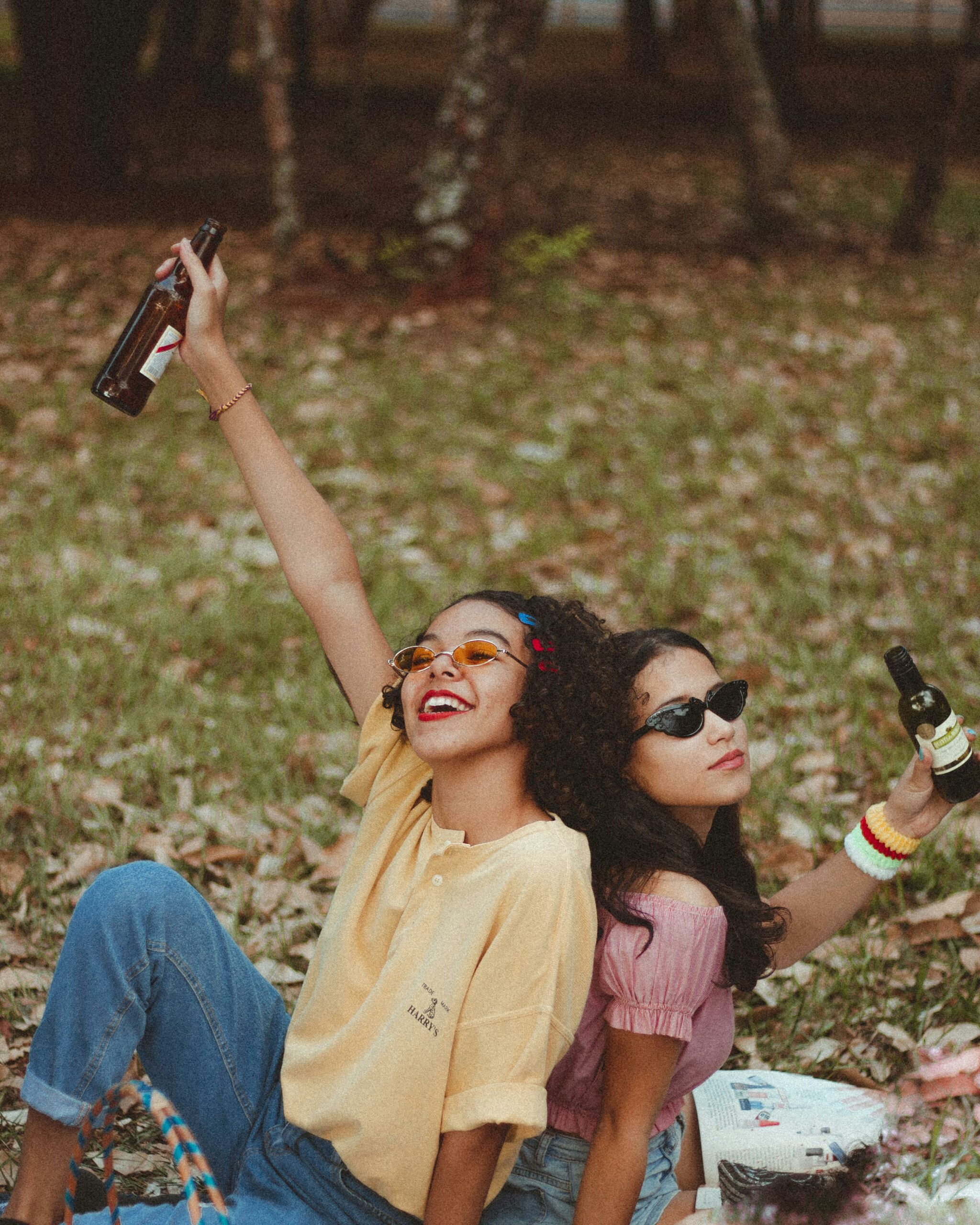 Two women enjoying a fun picnic in the park, raising drinks and celebrating friendship.