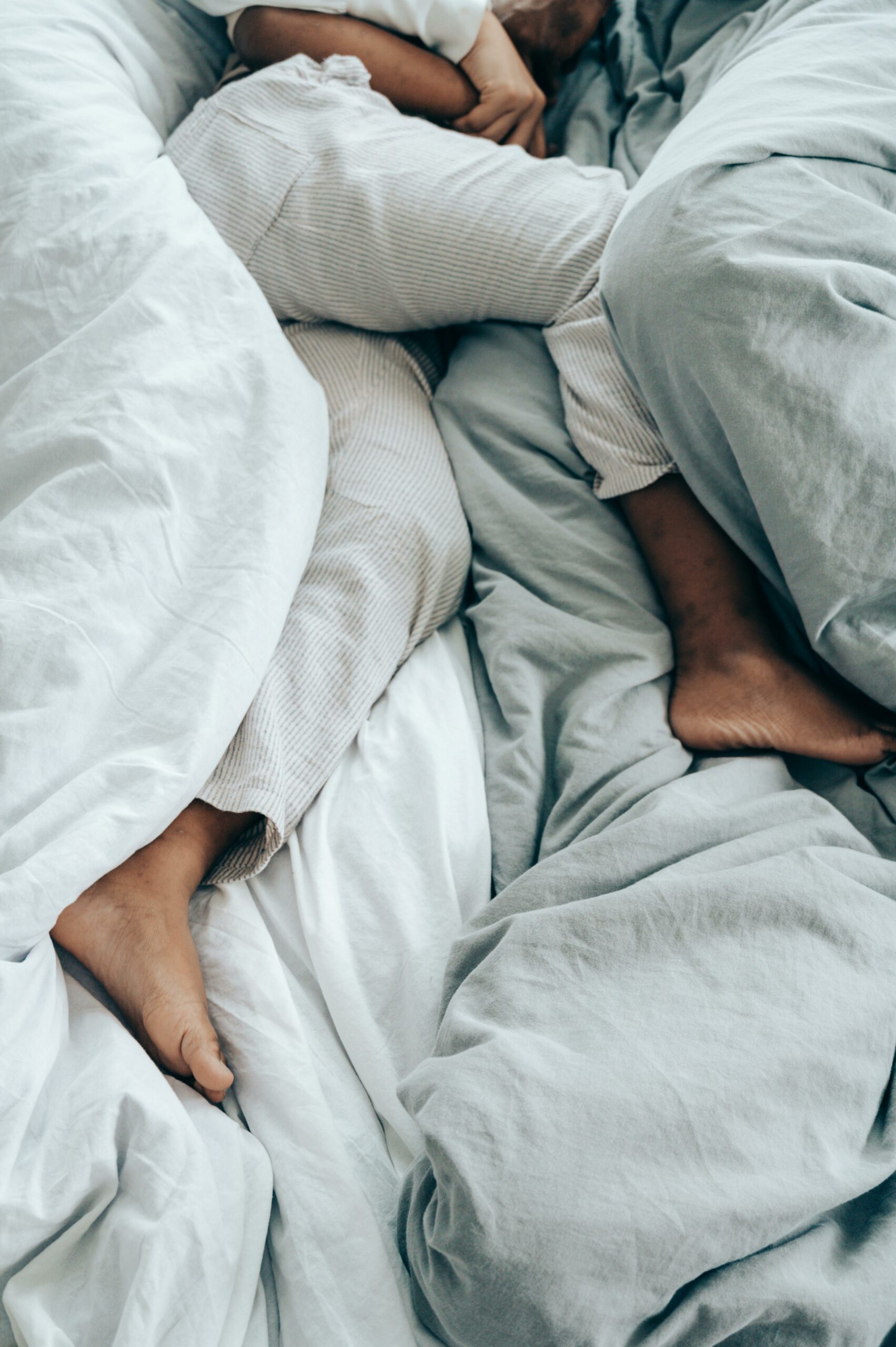 From above of crop unrecognizable person in pajama sleeping in comfortable soft bed